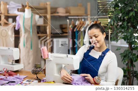 Repairwoman master is collecting and testing sewing machine after repairing sitting at table in sewing workshop 130314255