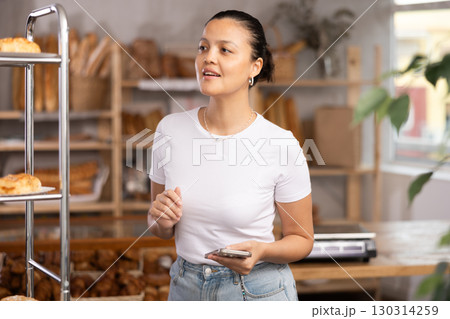 Middle-aged Asian woman chooses some pastry in bakery Middle-aged Asian woman chooses some pastry in bakery 130314259