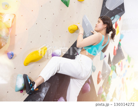 Young Asian woman climbs steep artificial wall in sports complex and trains endurance Young Asian woman climbs steep artificial wall in sports complex and trains endurance 130314272