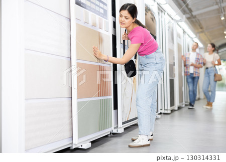 Positive woman wants to buy stone technical tiles for flooring or wall cladding in the materials department of hardware store 130314331