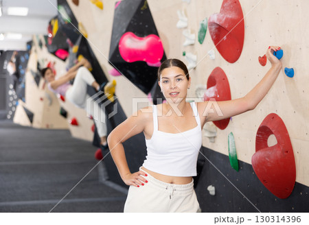 Smiling young girl posing near climbing wall at bouldering gym after workout, feeling accomplished and energized Smiling young girl posing near climbing wall at bouldering gym after workout, feeling accomplished and energized 130314396