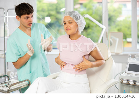 Young male doctor consulting female client on breast augmentation Young male doctor consulting female client on breast augmentation 130314410