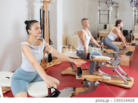 Young woman stretching her arms using pilates machine Young woman stretching her arms using pilates machine 130314428