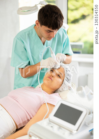 Young male cosmetologist doing ultrasound procedure to young woman Young male cosmetologist doing ultrasound procedure to young woman 130314550