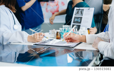 Medical team having a meeting with doctors in white lab coats and surgical scrubs seated at a table discussing a patients working online using computers 130315081
