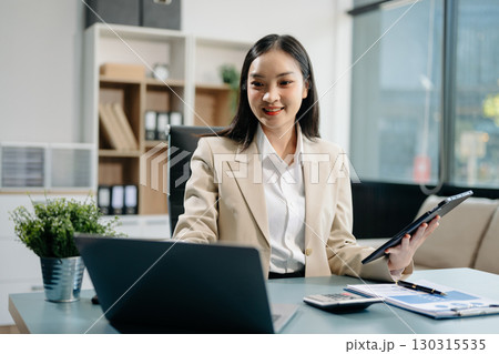 Confident business expert attractive smiling young woman typing laptop and holding digital tablet 130315535