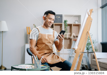 Asian male painter do artwork in art workshop, painting supplies, oil pastels, two canvas easel, creative space with paintbrush Asian male painter do artwork in art workshop, painting supplies, oil pastels, two canvas easel, creative space with paintbrush 130315804