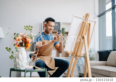 Asian male painter do artwork in art workshop, painting supplies, oil pastels, two canvas easel, creative space with paintbrush 130315818