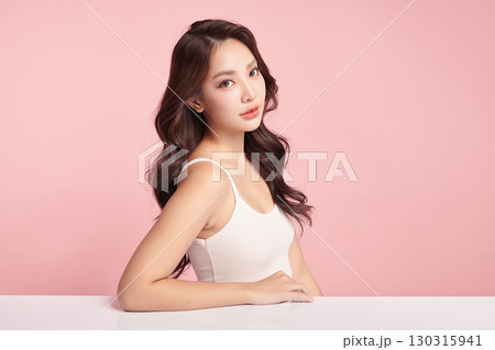 A beautiful young Asian woman with clean, fresh skin against a pink background. Skincare, facial treatment, cosmetology, beauty, and spa. An elegant portrait of an Asian woman. 130315941