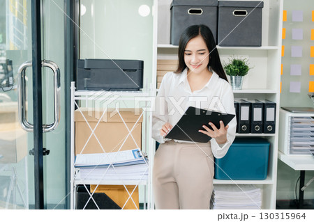 Asian businesswoman holding a pen taking note on note-paper attached to a mirror as a reminder laptop and tablet on the desk. 130315964