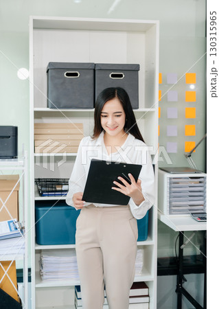 Asian businesswoman holding a pen taking note on note-paper attached to a mirror as a reminder laptop and tablet on the desk. 130315965