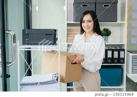 Happy and excited young beautiful Asian woman office worker celebrating her resignation, carrying her personal stuff. leaving job, changing or company. 130315969