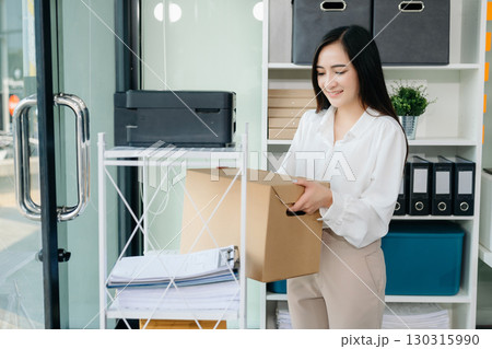 Happy and excited young beautiful Asian woman office worker celebrating her resignation, carrying her personal stuff. leaving job, changing or company. 130315990