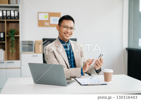 Young handsome man typing on tablet and laptop while sitting at the working table office Young handsome man typing on tablet and laptop while sitting at the working table office 130316483