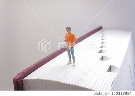 Miniature Figure Standing on a Large Book Pages Edge 130318984