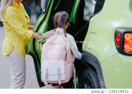 Mother helps daughter get into car for the school run, showing family support, safety, and back to school morning routine. Mother helps daughter get into car for the school run, showing family support, safety, and back to school morning routine. 130319432