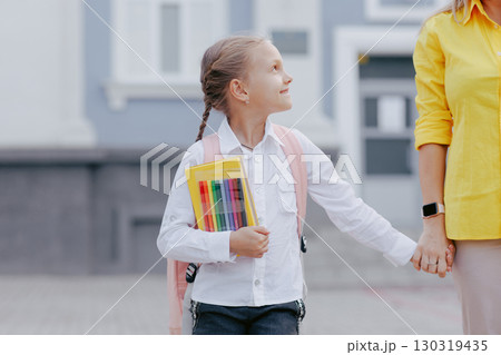 Happy student girl with school backpack and stationery holds hands with mom, excited for the first day back to school. 130319435
