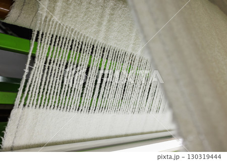 Woolen fabric weaving in progress on an industrial loom, showcasing textile production and manufacturing process closeup. 130319444