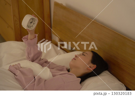 深夜に布団の中で時計を見ている女性 130320183