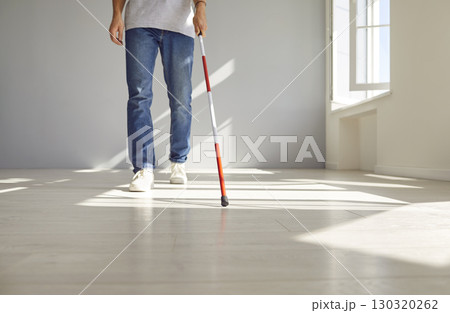Deaf and visually impaired man is walking with a red white cane indoors, at home Deaf and visually impaired man is walking with a red white cane indoors, at home 130320262