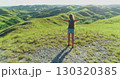 Young woman tourist embracing freedom on Sumba Island, Indonesia, with arms outstretched in an idyllic landscape of lush green hills, basking in the warm glow of sunset 130320385