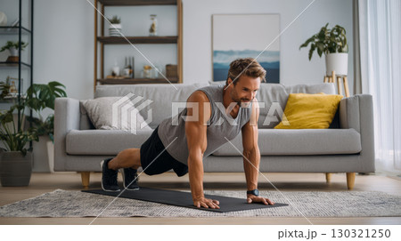 Man exercising at home doing push up on yoga mat in living room with modern decor and natural light 130321250