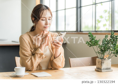 カフェでコーヒーを飲みながらスマホを見る若いアジア人女性（待ち合わせ） 130322194