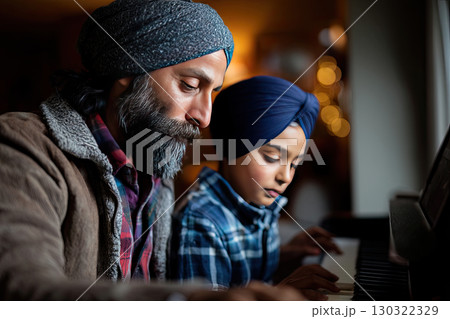 Side-view of a mid adult father teaching his real young son how to play the piano. The father and son are Sikh, and they are both wearing turbans with casual clothing 130322329