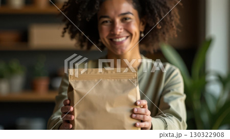 Cheerful young African American woman holding out a brown paper bag mock-up. 130322908