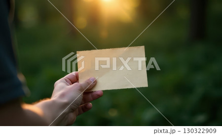 A Hand Gracefully Holding a Blank Paper in Front of a Blurred Forest During a Beautiful Sunset. Mock-up A Hand Gracefully Holding a Blank Paper in Front of a Blurred Forest During a Beautiful Sunset. Mock-up 130322909