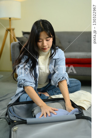 Happy woman sits on carpet folding sweater and packing neatly into suitcase Happy woman sits on carpet folding sweater and packing neatly into suitcase 130322967