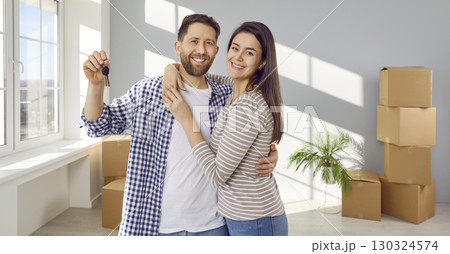 Married smiling couple buying their new home. Happy family couple in casual clothes received the keys to their new modern apartment and show them on camera. Real estate, moving, renting, own housing. 130324574