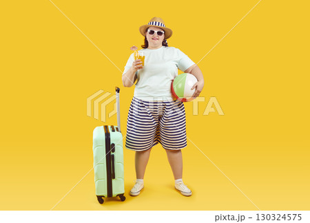 Fat woman with holiday suitcase, beach ball and cocktail standing on yellow background 130324575