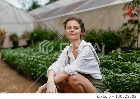 Young woman in a greenhouse, wearing a casual outfit, smiling amidst lush greenery, symbolizing a connection with nature and healthy living 130325302