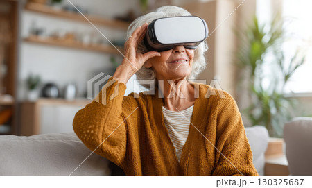 Concept of futuristic technology and fun from the elderly - Mature woman sitting on the sofa at home having entertainment and playing with virtual reality - Happy retired uses vr glasses 130325687