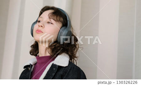 A girl listens to music or audio with headphones, her peaceful expression suggesting deep engagement. The photo symbolizes the transformative power of sound in creating moments of clarity. 130326226