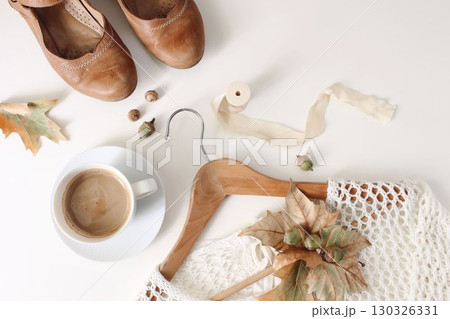 Autumn flatlay with leather shoes, coffee cup, wooden hanger, knitted sweater, acorns and dried leaves isolated on white background. Cozy fashion scene, neutral tones. Fall lifestyle composition, top 130326331
