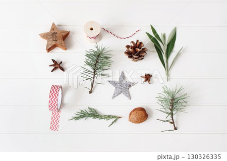 Natural Christmas composition. Pine branches, stars, pinecone, almond. Star anise, greenery decoration. Red string spool, festive ribbon. White wooden rustic table background. Flatlay, top view 130326335