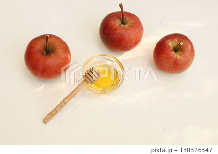 Autumn seasonal still life scene. Red apples, bowl of honey, wooden dipper isolated on beige table background in sunlight. Fall, Rosh Hashanah, Thanksgiving holiday banner. Gardening. Flatlay top view Autumn seasonal still life scene. Red apples, bowl of honey, wooden dipper isolated on beige table background in sunlight. Fall, Rosh Hashanah, Thanksgiving holiday banner. Gardening. Flatlay top view 130326347