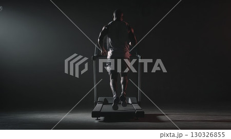 Determined male athlete running on treadmill in dark gym 130326855