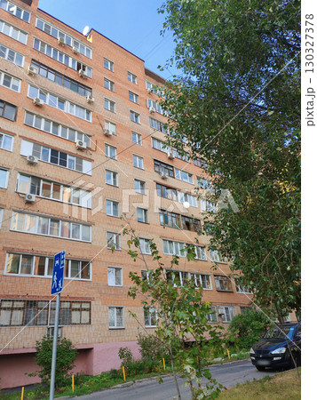 A tall red and beige brick residential building with multiple balconies, air conditioning units, and a sidewalk below. The structure reflects the typical architecture of urban apartment blocks in 130327378