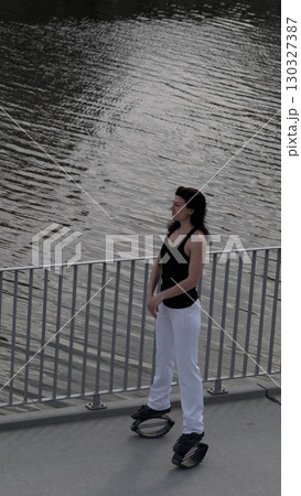 A confident woman practices rebound jumping near a river, using special spring-loaded boots. Fitness innovations like these help make exercise more dynamic and accessible to all ages. 130327387