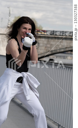 A fit woman smiles while raising her fists in a defensive boxing position, exuding energy and determination. The modern fitness trend embraces martial arts as a way to build confidence and mental 130327388