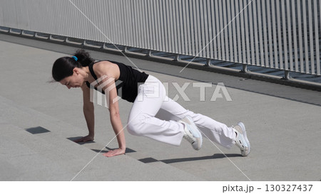 A woman performs mountain climbers on an outdoor concrete surface, focusing on endurance and core strength. This image highlights dedication to fitness and high-intensity exercise. 130327437