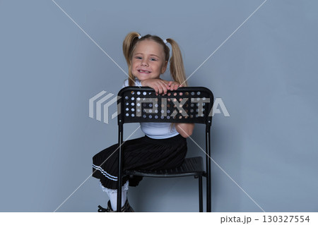 A happy 5-year-old girl, dressed in a stylish skirt and boots, is captured laughing while leaning on a chair in a studio setting. The photo showcases her playful side, perfect for children's 130327554