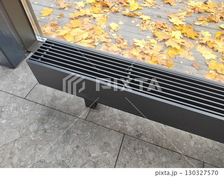 A modern floor heating vent near a glass window with autumn leaves scattered outside. The photo combines indoor functionality with the charm of seasonal outdoor scenery. 130327570