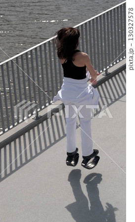 A woman in Kangoo Jumps boots jumps gracefully along a waterfront promenade, her hair moving with the motion. The rise of alternative fitness methods highlights the modern trend of making exercise 130327578
