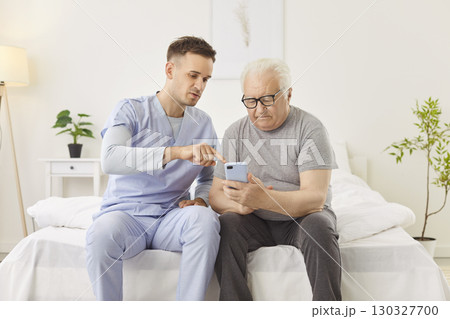 Young nurse sitting with senior man and teaching him to handle with mobile phone in medical clinic 130327700