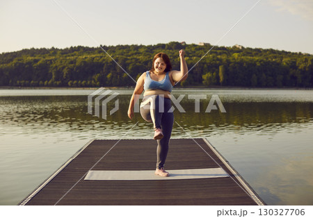 Happy young overweight woman in sportswear having fitness workout on river jetty Happy young overweight woman in sportswear having fitness workout on river jetty 130327706