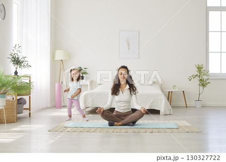 Happy calm mother resting in lotus pose, breathing techniques, mindfulness practice with daughter Happy calm mother resting in lotus pose, breathing techniques, mindfulness practice with daughter 130327722
